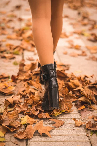 Feet of a woman in heels in autumn in a park with brown leaves on the ground