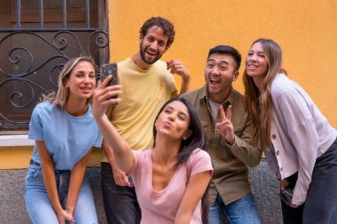 Bir grup çok ırklı arkadaş şehirde gülümseyerek selfie çekiyor.