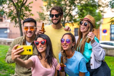 Şehir parkında eğlenen çok ırklı arkadaş grubu güneş gözlüklü selfie, arkadaşlık ve eğlence konsepti çekiyorlar.