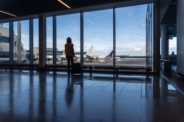 Havaalanı terminalinde bavullu bir kadın uçağı bekleyen uçaklara bakıyor.