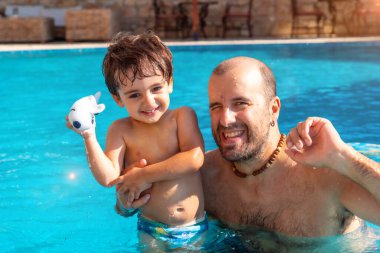 Yazın yüzme havuzunda baba ve oğulun portresi tatilde eğleniyor ve gülümsüyor.