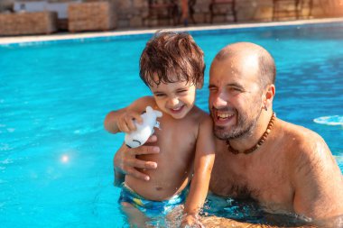 Baba oğul yazın havuzda eğleniyor ve gülümsüyor.