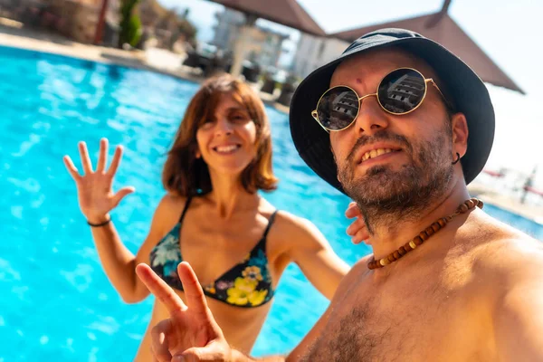 Tourist couple in the hotel pool in summer taking a selfie enjoying the vacation