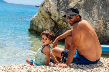 Lefkada 'daki Paralia Mikros Gialos plajında oynayan baba-oğul portresi. Taş atıyorlar. Yunanistan.