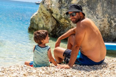 Lefkada 'daki Paralia Mikros Gialos plajında oynayan baba-oğul portresi. Taş atıyorlar. Yunanistan.