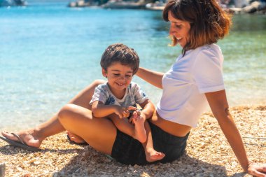 Anne oğul, Yunanistan 'ın Kefalonia adasındaki Fiskardo sahilinde bir plajda gülümsüyor.