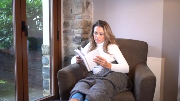 Μια Νεαρή Ξανθιά Λευκή Γυναίκα Διαβάζει Ένα Βιβλίο Στη Ζεστασιά — Αρχείο Βίντεο