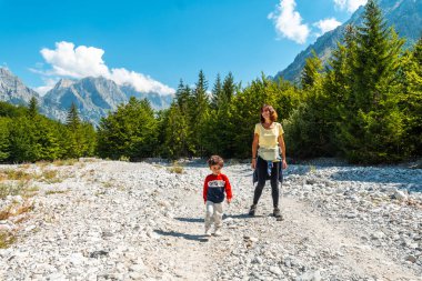 Oğluyla Valbona Vadisi 'nde ağaçların, Theth Ulusal Parkı, Arnavut Alpleri ve Arnavutluk' un yanındaki patikada yürüyen bir turist