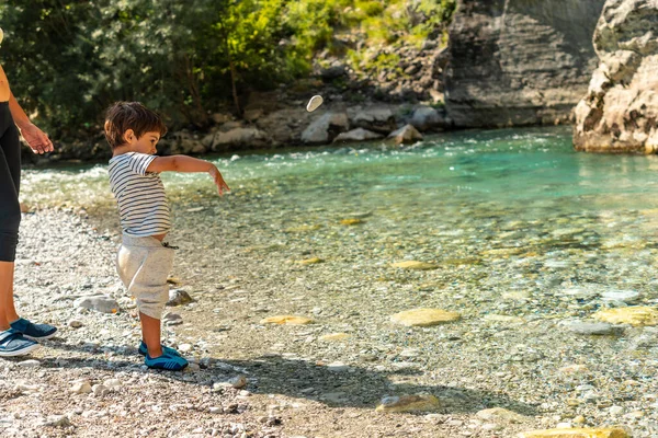 A boy playing and throwing stones in the turquoise river of the Valbona valley, Theth national park, Albanian Alps, Albania