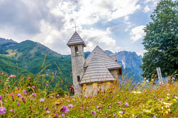 The beautiful Catholic Church in the valley of Theth national park with pink flowers, Albania. albanian alps