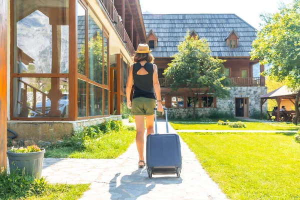 Tourist woman with a suitcase on rural vacation arriving at a mountain cabin