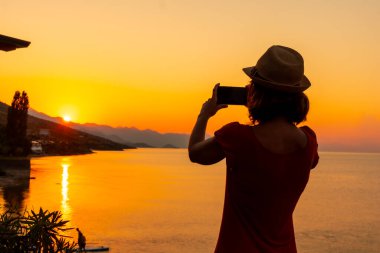 Shiroka belediyesinin Shkoder Gölü 'nde yaz tatilinde gün batımında fotoğraf çeken bir kadının silueti. Arnavutluk