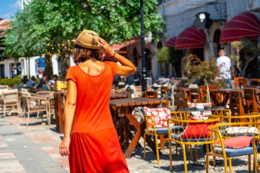 Kırmızı elbiseli ve şapkalı turist kadın Shkoder şehrinin sokaklarında tatilin tadını çıkarıyor. Arnavutluk