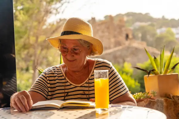 Happy elder woman reading a book in an outdoor terrace with views of the nature