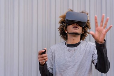 Sokak stili gri arka planlı yatay fotoğraf. Sanal gerçeklik gözlüğü kullanırken hareket eden genç adam.