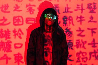 Çince kelimelerle dolu bir duvarda AR gözlükleri olan fütürist bir adamın kırmızı neon ışıkları olan stüdyo portresi.