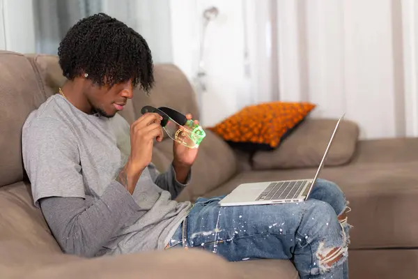 Side view of a young african man sitting at home using laptop and AR goggles
