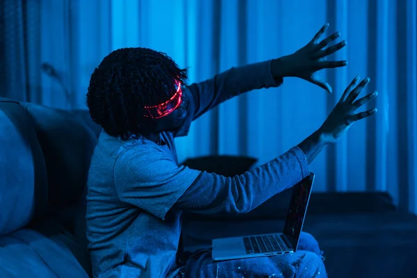 Afro man playing with laptop and Augmented reality goggles in a living room with neon blue light
