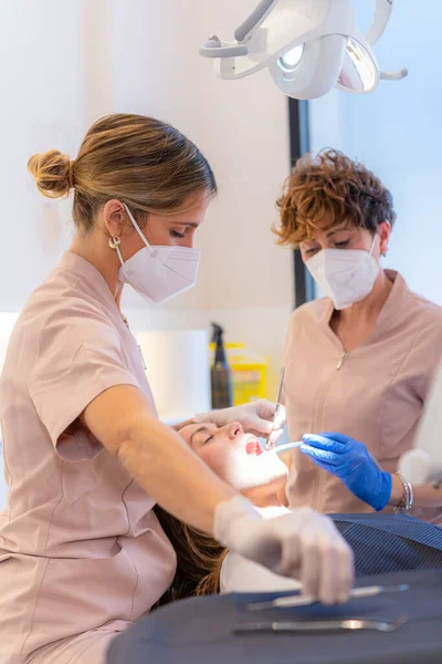 Vertical photo of a technician examining the teeth of a woman reclining on chair