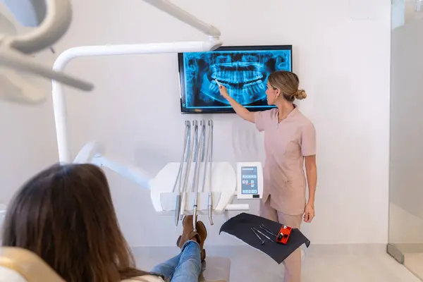 Dentist showing the results of the scan to a patient sitting on a chair in the clinic