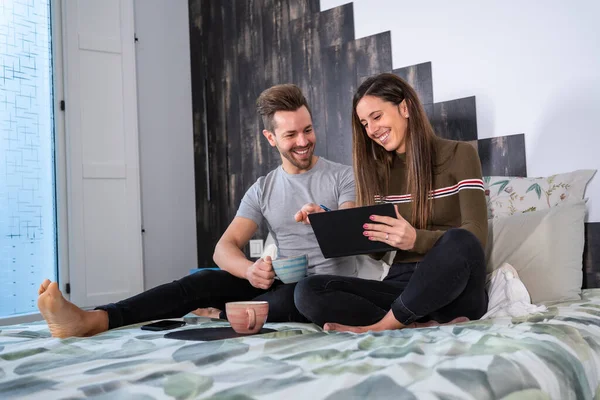 情侣们早上坐在床上 用平板电脑 喝咖啡 — 图库照片