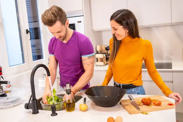 Horizontal photo of a happy couple washing the ingredients for a salad at home