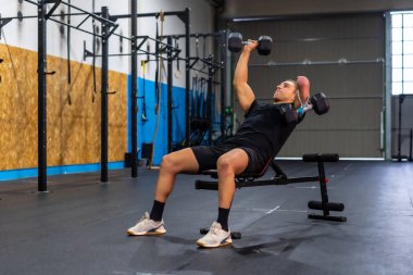 Kolu kesilmiş engelli güçlü bir adam spor salonunda dambıllarla egzersiz yapıyor.