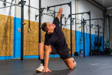 Kolu kesilmiş bir adam, spor salonunda tek başına esneme hareketleri yapıyor.