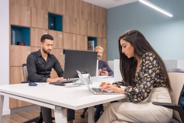 Ciddi bir kadın iki erkeğin yanında çalışırken dizüstü bilgisayar kullanıyor.