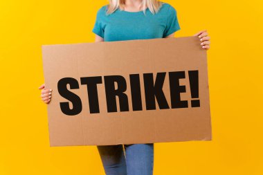 Hollywood oyuncuları ve yazarlarının sloganıyla bir pankartı protesto eden bir kadın sarı arka planda grev yaptı.