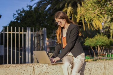 Sıradan bir iş kadınının binanın dışında dizüstü bilgisayar kullanırken çekilmiş yatay bir fotoğraf.