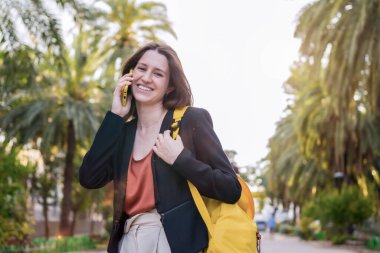 Gülümseyen sıradan bir kadın parkta yürüyen cep telefonuyla konuşuyor.