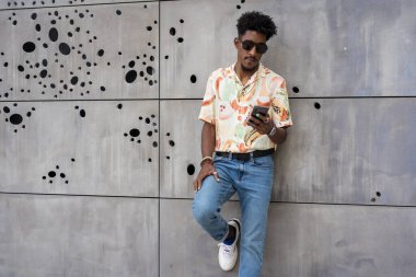 Telefonunu kullanan sıradan esmer bir adam duvarda rahatça duruyor.