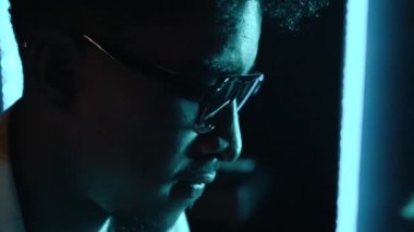 Konsantre ses mühendisi ya da yapımcı mavi LED ışıkla müzik kayıt stüdyosunda çalışıyor. Güneş gözlüklü zenci bir müzisyen.