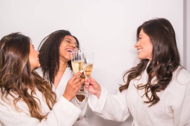 Beyaz arkaplanlı stüdyo fotoğrafı. Çok ırklı üç arkadaş şampanya ile hayatı kutluyor.