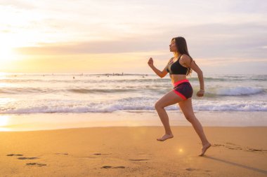 Gün batımında kumsalda koşan genç bir kadın.