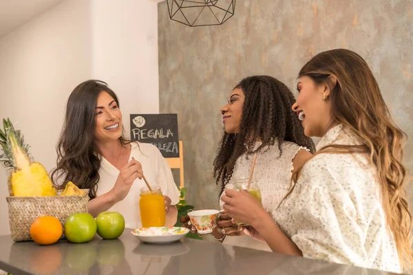 Three latin female friends enjoying healthy snacks and juices in a cafeteria