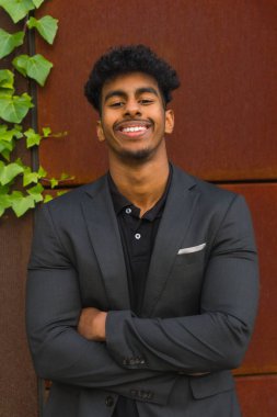 Kollarını kavuşturarak kameraya gülümseyen başarılı genç bir girişimcinin dikey portresi.