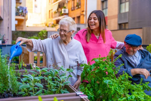 Happy retired elder people watering plants in a geriatric next to the supervision of a nurse