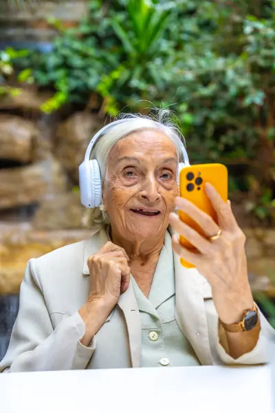 Vertical portrait of a elder woman listening to music using phone in a geriatric