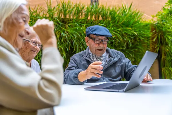 Happy elder people using laptop sitting on a garden in a nursing home