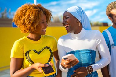 Açık havada telefon kullanan iki Afro-Amerikan genç kadının ön mutlu portresi.