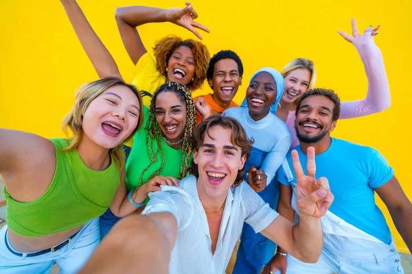 Young people from different ethnicities taking a happy selfie at a gathering next to a yellow background