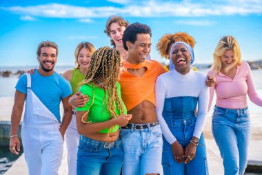 Mutlu bir transseksüel ve çok ırklı bir arkadaşın gezinti güvertesinde yürürken kucaklaşması ön planda.