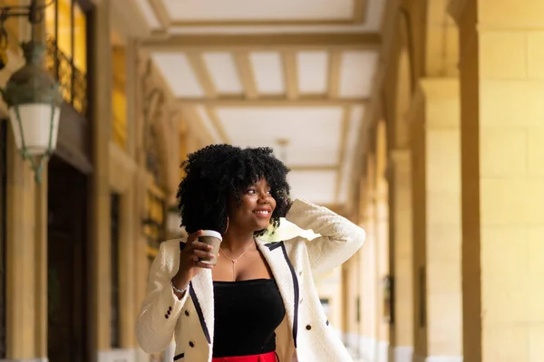 Elegant african businesswoman walking with a take away coffee next to a beauty modern building