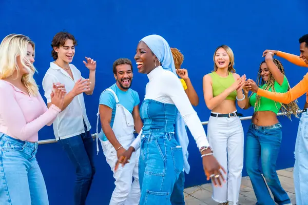 Muslim young woman dancing in a dance battle with friends with a blue wall as background