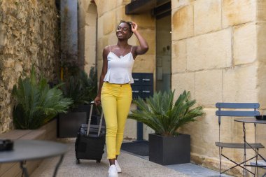 Antik bir caddede bavuluyla yürüyen Afrikalı genç bir kadının fotokopisi.