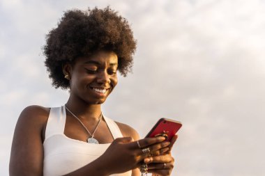 Gün batımında dışarıda telefon kullanan Afrikalı bir kadının düşük açılı portresi.