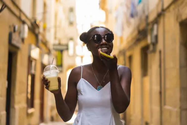 Frontal portrait of a young african woman enjoying a milkshake in the street