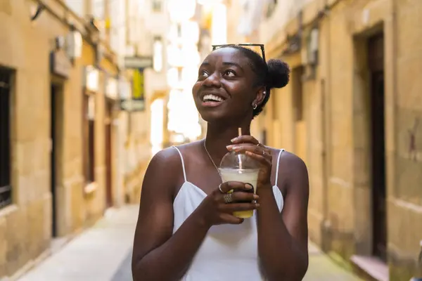 African woman looking up with amazed expression while drinking a take away milkshake visiting a city